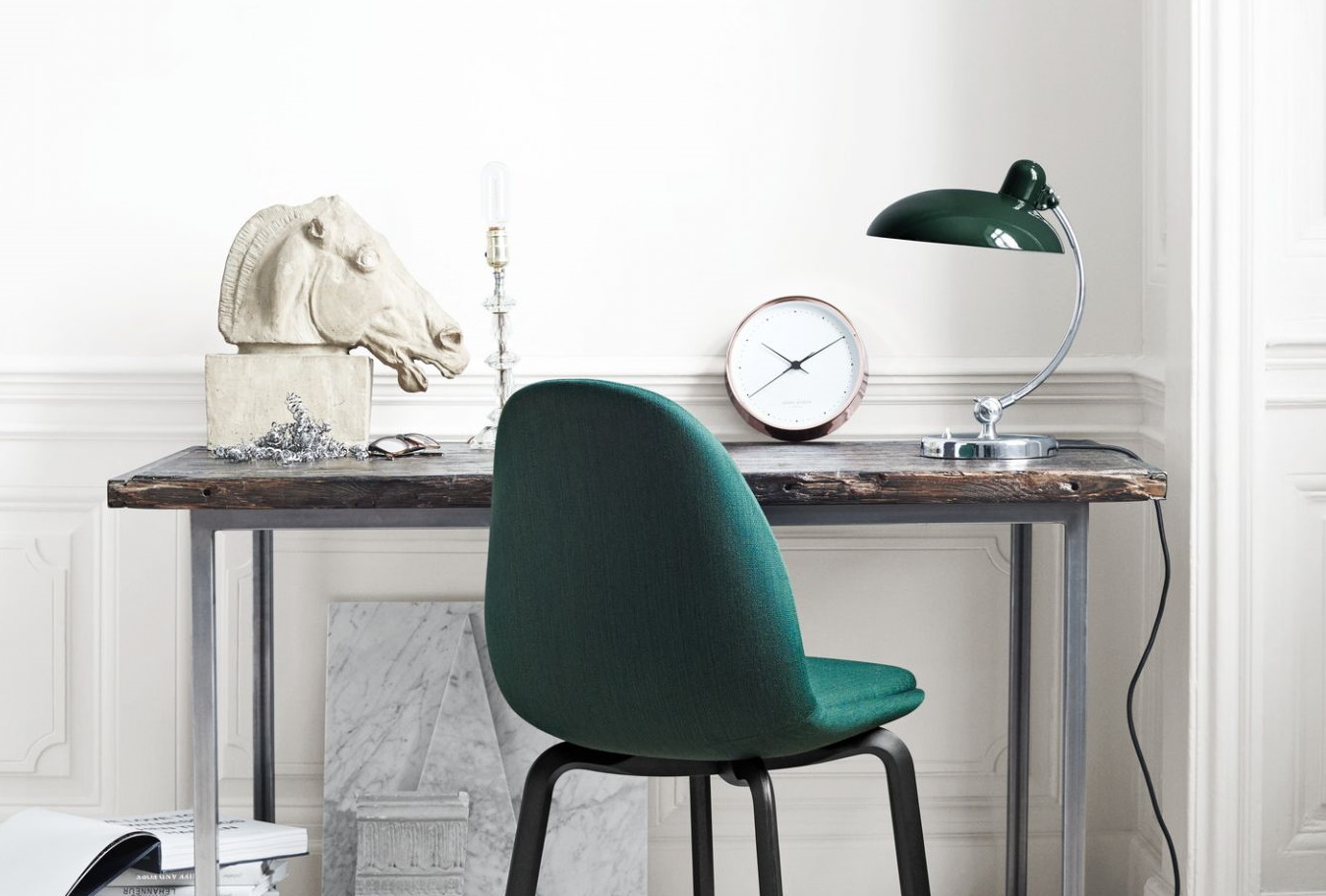 Grüner Stuhl am Schreibtisch mit Lampe, Uhr und Pferdekopf-Skulptur. Büro- und Arbeitszimmer-Einrichtung.