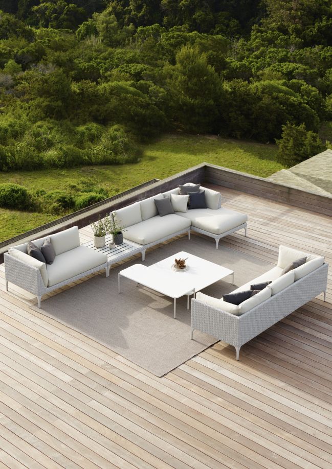 Weißes Outdoor-Lounge-Set mit Sofa, Sessel und Tisch auf einer Holzterrasse mit Blick ins Grüne.