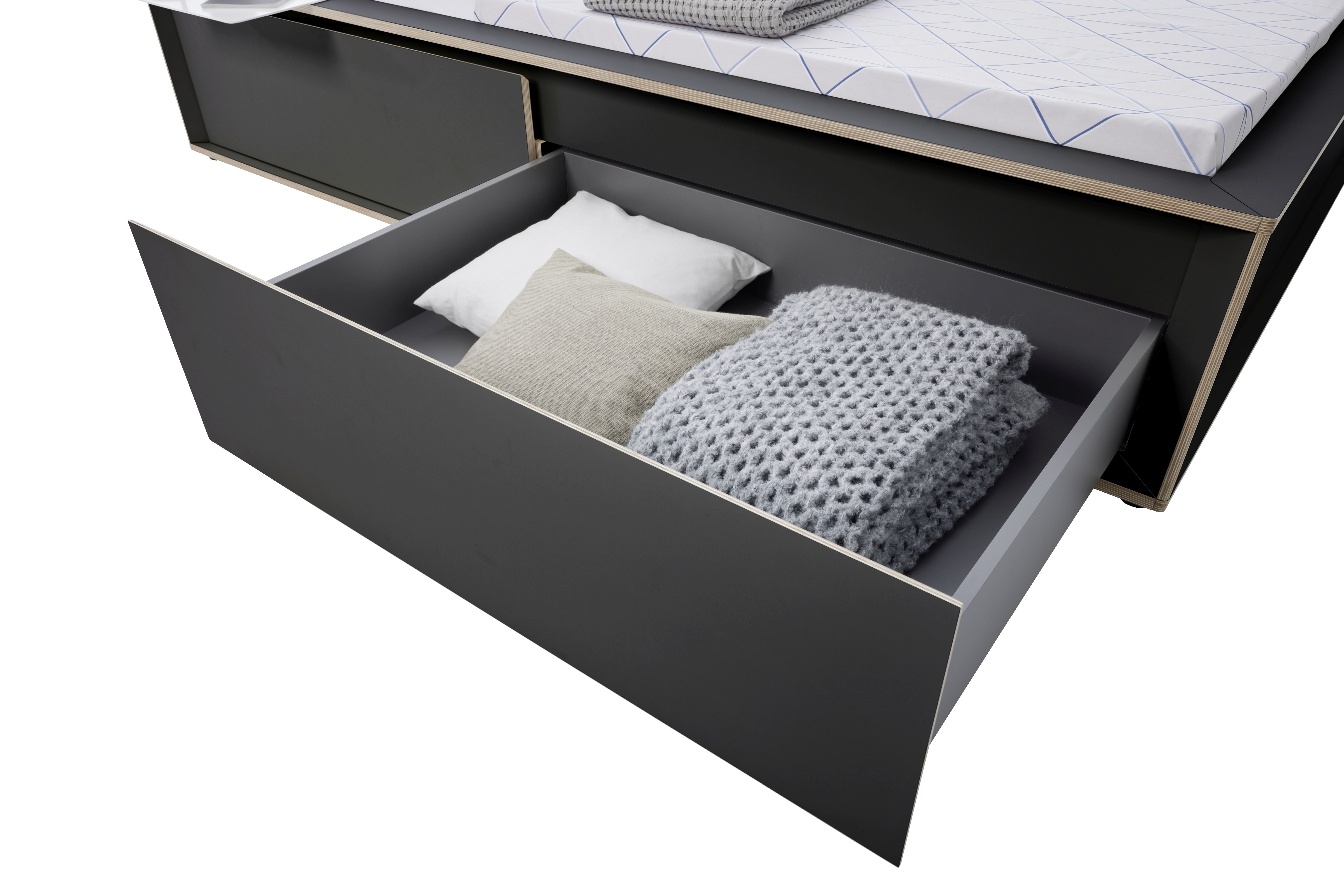 Spaze Bett von Müller Möbelwerkstätten mit offener Schublade, Kissen und grauer Strickdecke.