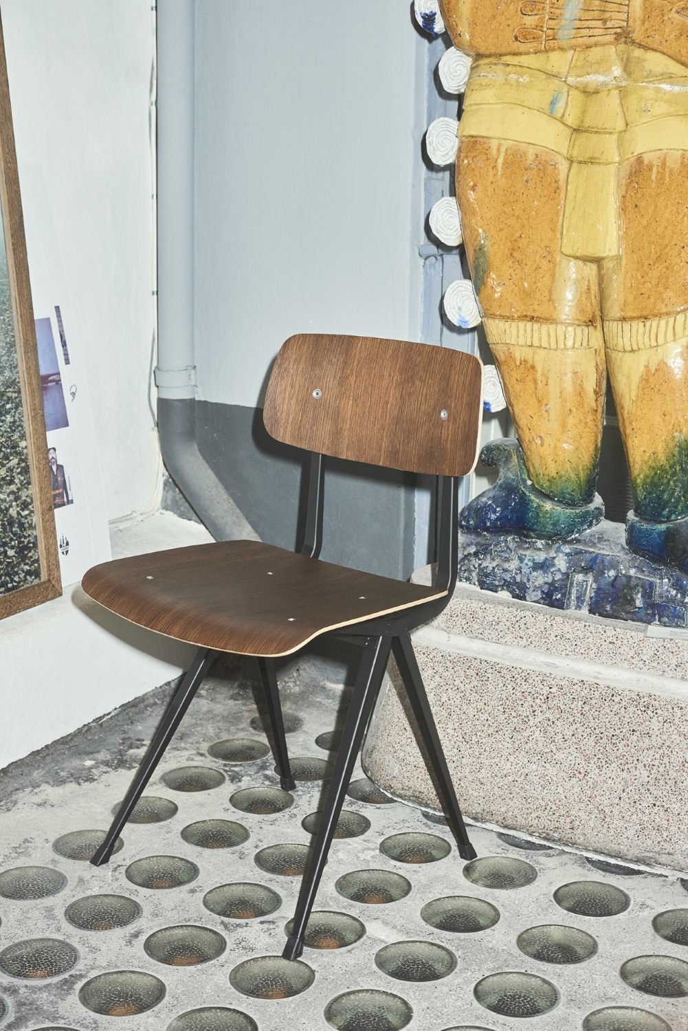 Hay Result Chair Stuhl mit dunklem Holz und schwarzem Metallgestell vor ungewöhnlichem Hintergrund.