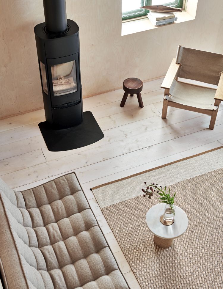 Beige Pappelina Teppich Edit im Wohnzimmer mit Kamin, Sessel und Sofa, skandinavisches Design.