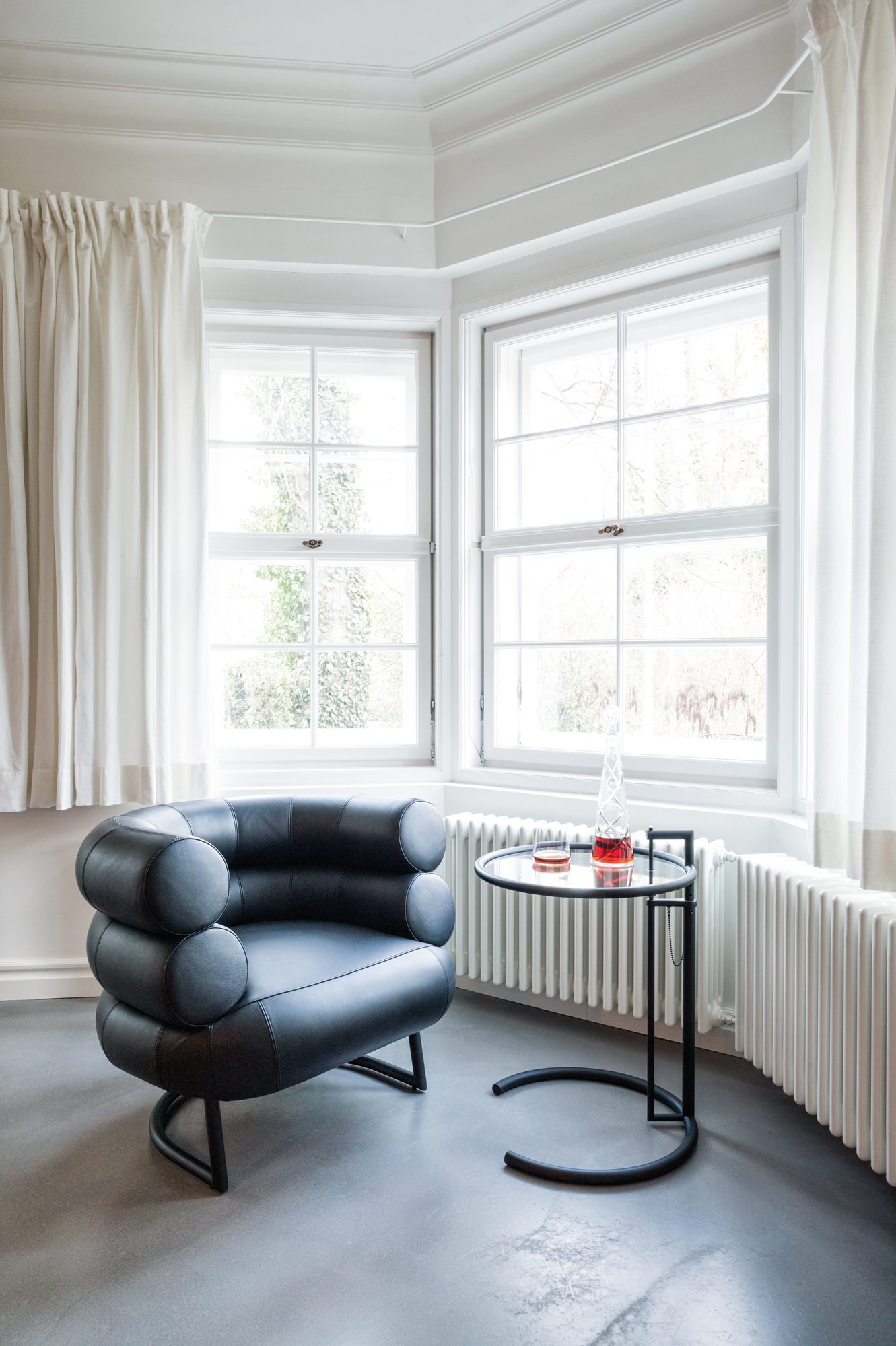 ClassiCon E1027 Beistelltisch, schwarzes Gestell mit Kristallglasplatte, neben einem schwarzen Sessel.