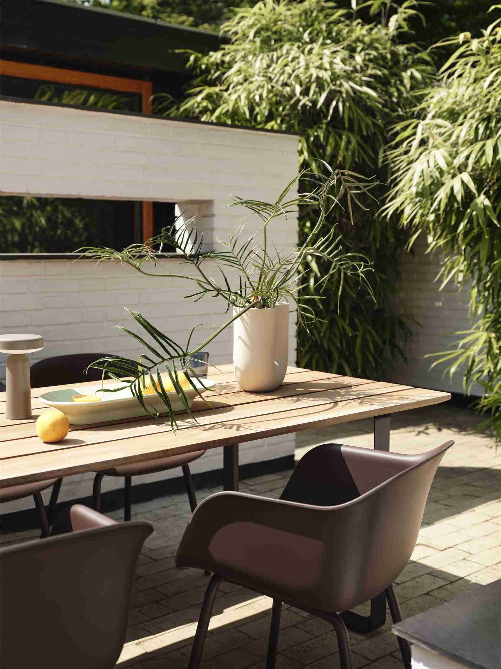 Muuto Kink Vase Sand, eine moderne Blumenvase aus Keramik, dekoriert einen Holztisch im Garten.
