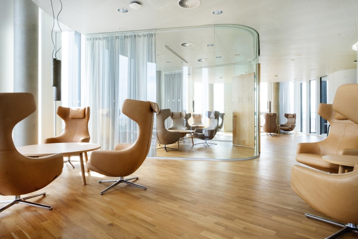 Helle Bürolounge mit mehreren braunen Vitra Grand Repos Sesseln und Holzboden für entspanntes Sitzen.