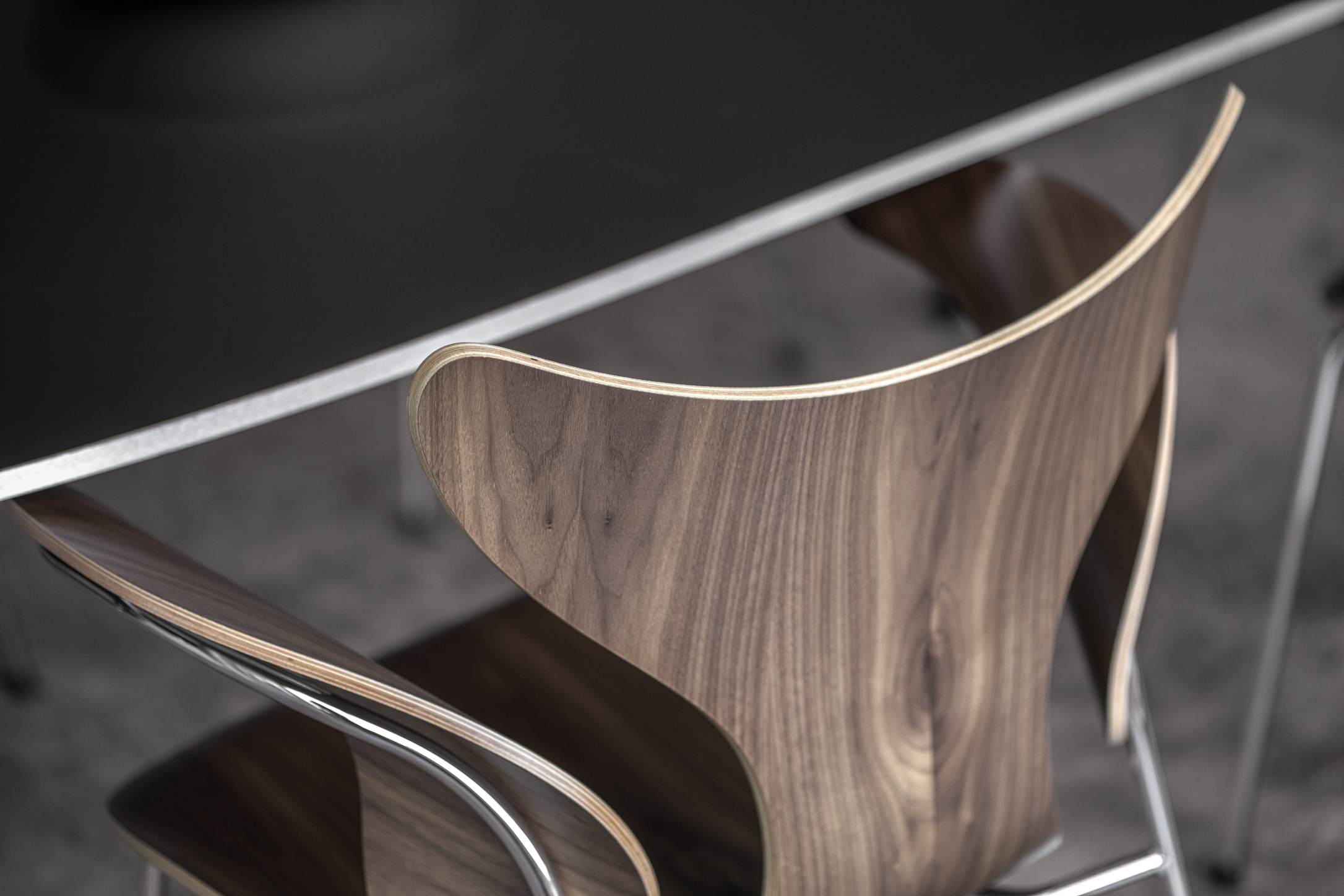 Detailaufnahme des Fritz Hansen Lily Stuhls mit Armlehne aus Walnussholz und verchromtem Stahlgestell.