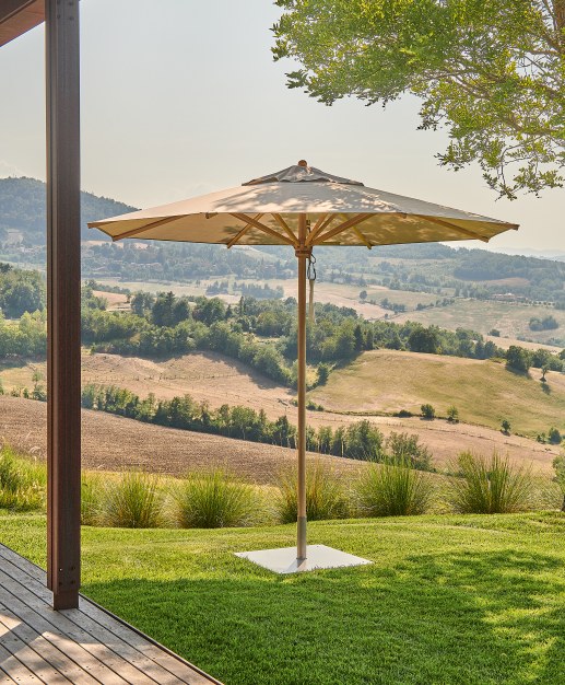 Weishäupl Klassiker Sonnenschirm mit Holzgestell und beigem Schirmstoff im Garten mit Blick auf hügelige Landschaft.