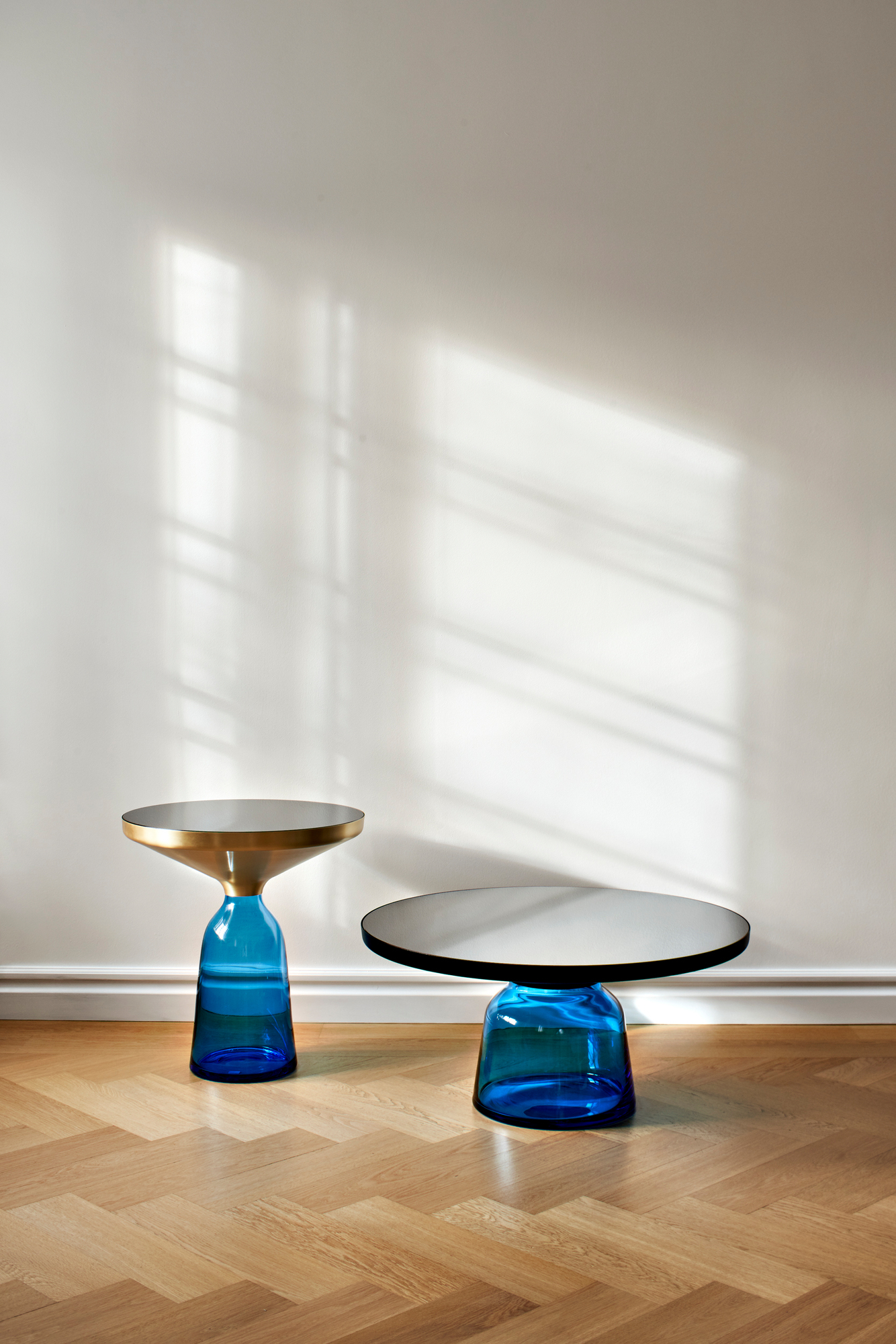 Zwei ClassiCon Bell Side Tables mit Marmor Tischplatte und blauem Glasfuß auf Parkettboden.