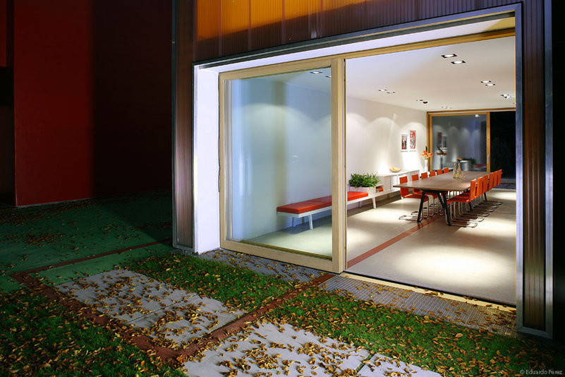 Innenansicht eines modernen Esszimmers mit langem Holztisch und roten Vitra .05 Stühlen.