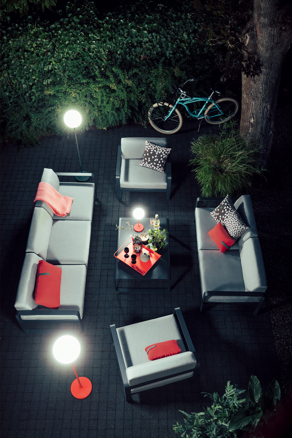 Bellevie Fermob Sessel und Outdoor-Möbel-Set auf dunklem Pflaster mit Beleuchtung und Fahrrad im Hintergrund.
