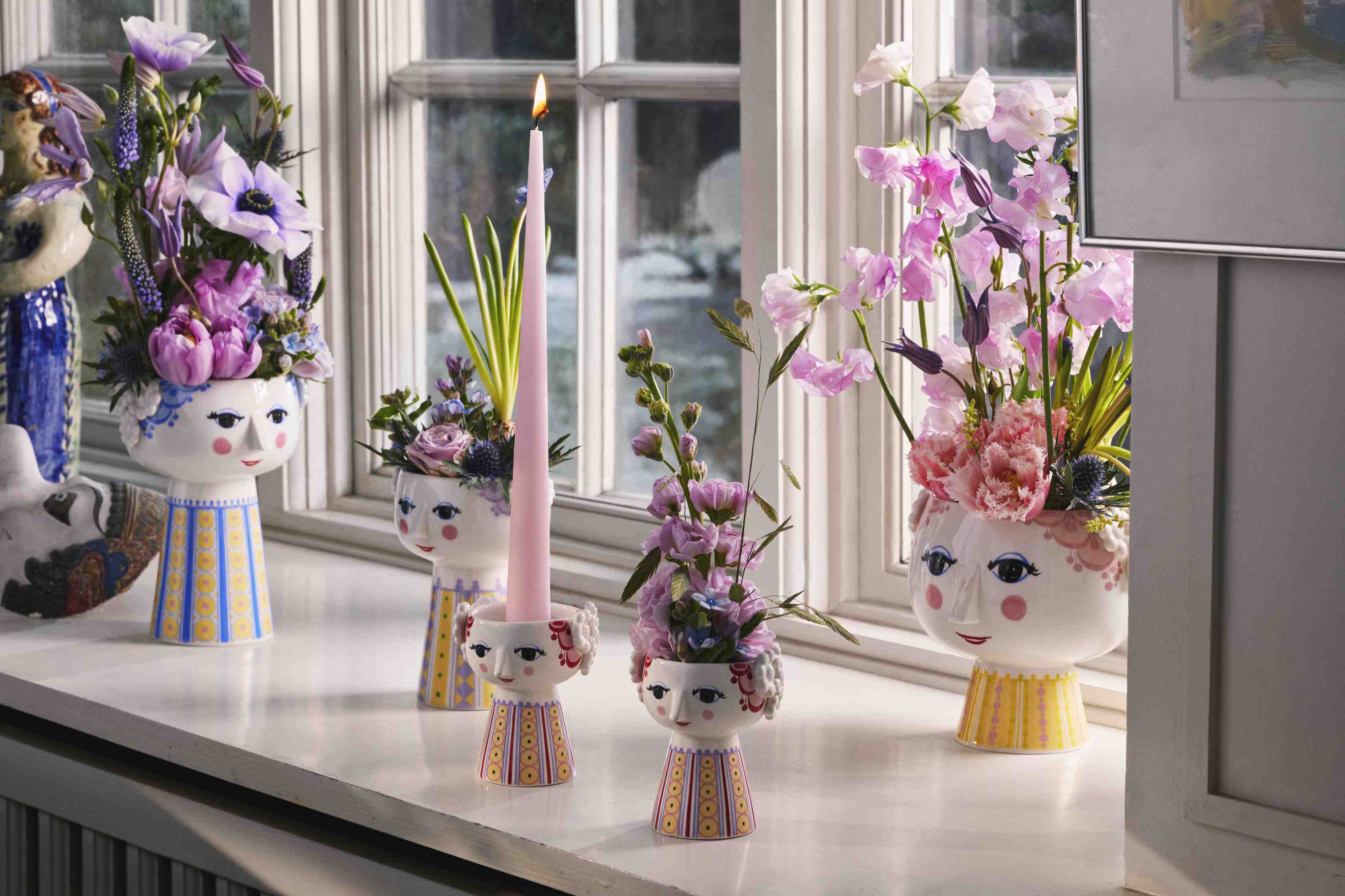 Keramik-Blumenvasen mit Gesicht und bunten Blumen auf einer Fensterbank, dekorative Wohnaccessoires für ein stilvolles Zuhause.