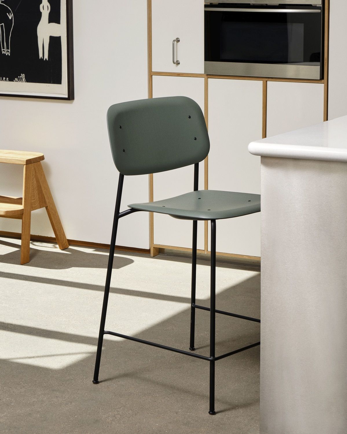 Hay Soft Edge 90 Barhocker in Grün mit schwarzem Gestell vor Küchenzeile.
