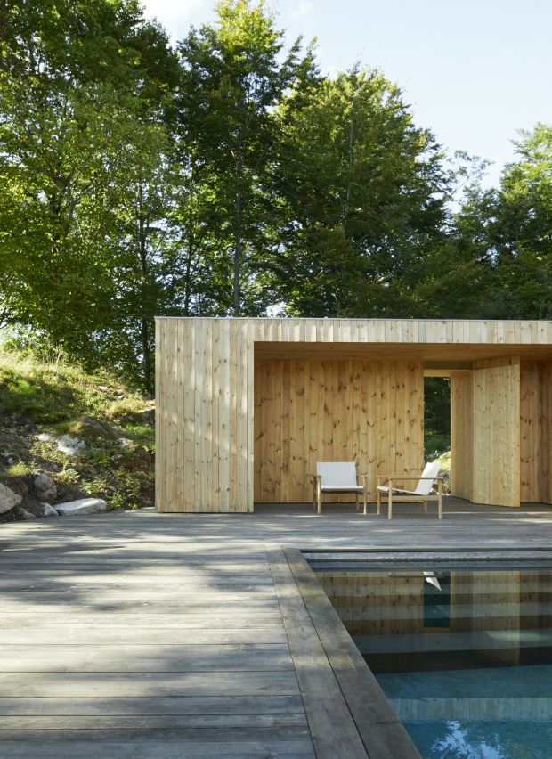 Zwei Pelagus Lounge Sessel von Skagerak by Fritz Hansen auf Holzterrasse neben Pool und Holzhütte.