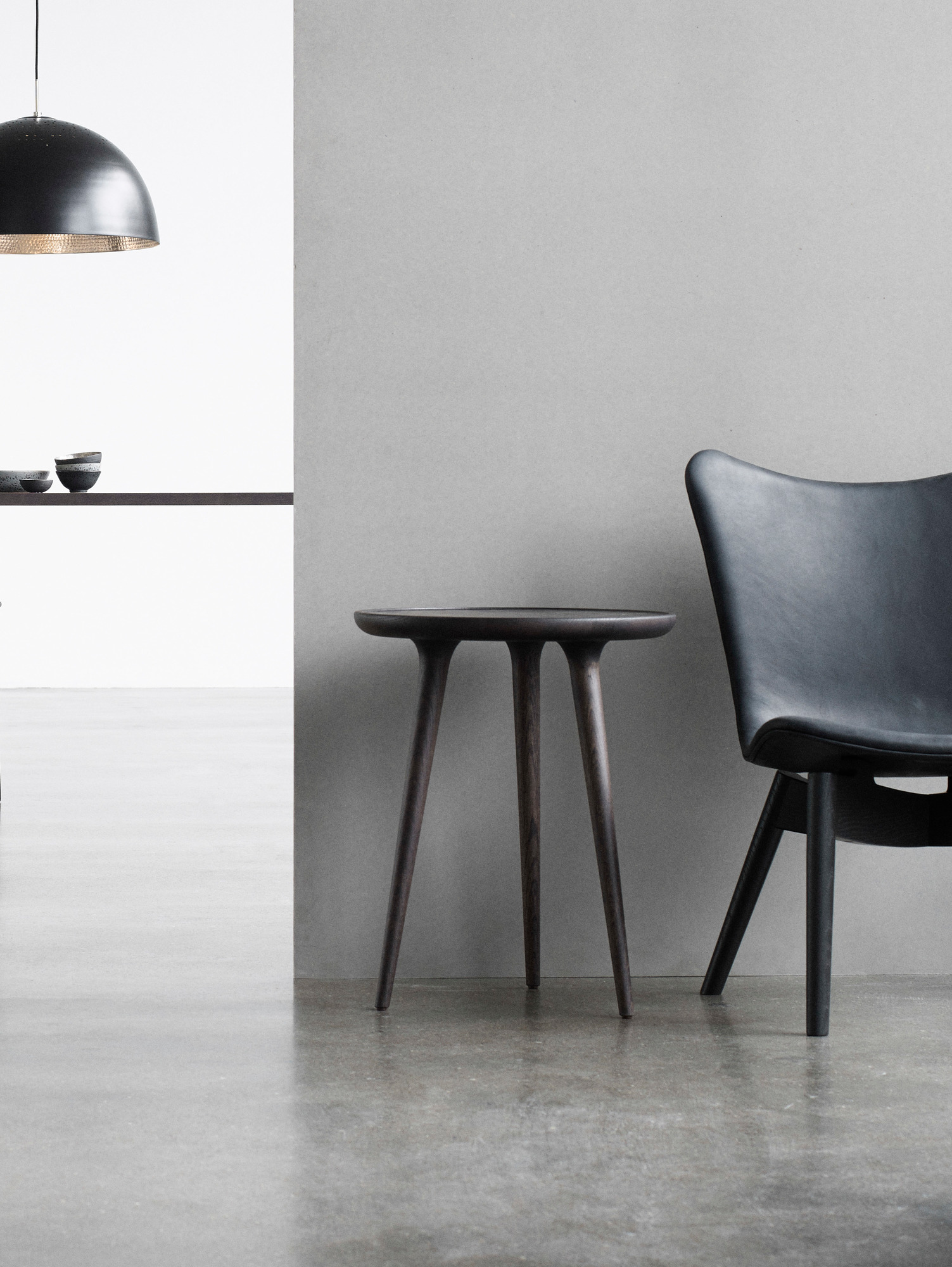 Dunkler Mater Accent Side Table Beistelltisch Medium neben einem schwarzen Sessel auf grauem Untergrund.