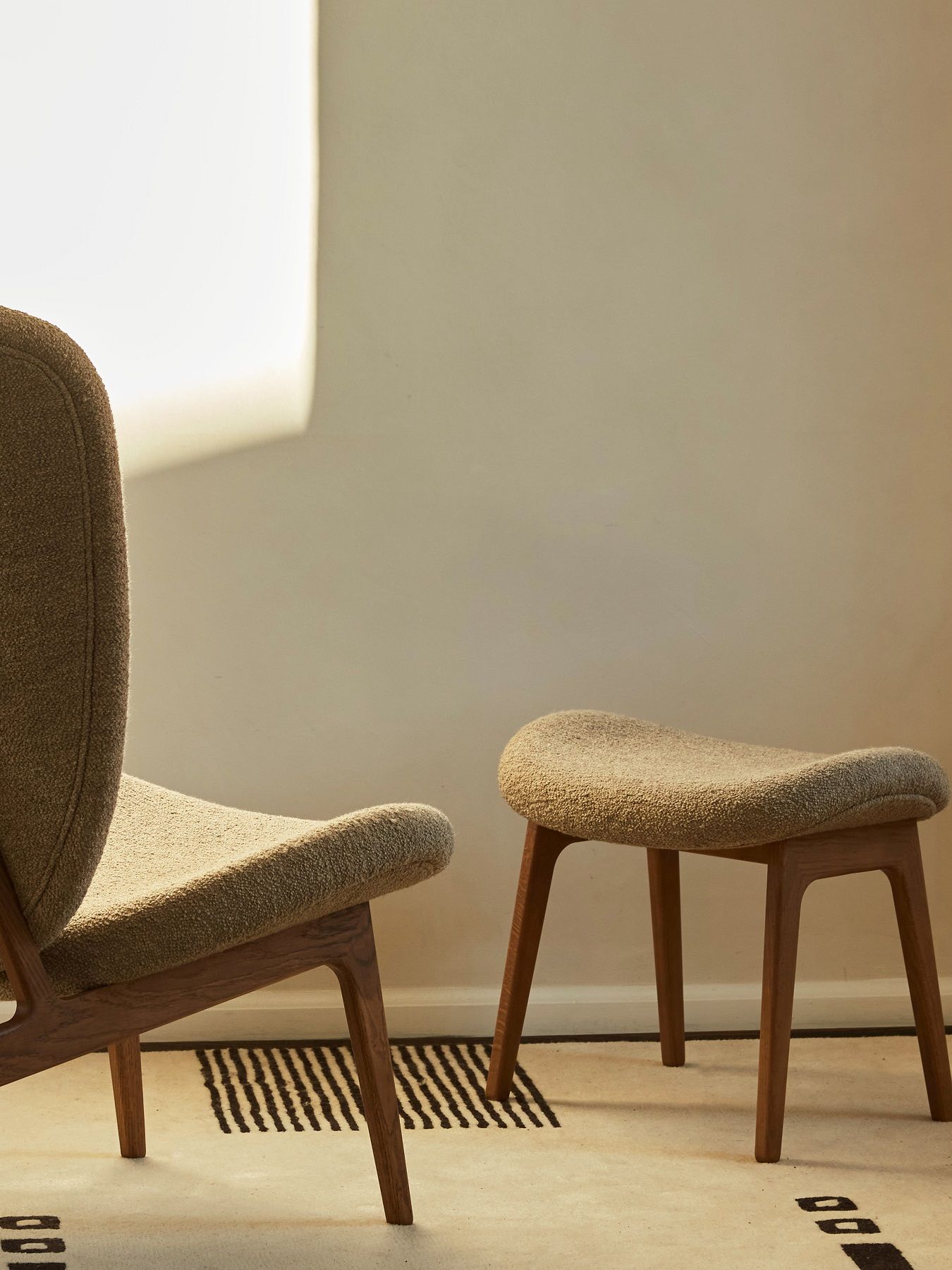 Nahaufnahme des NORR11 Elephant Lounge Sessels mit passendem Hocker, beige Stoffbezug.