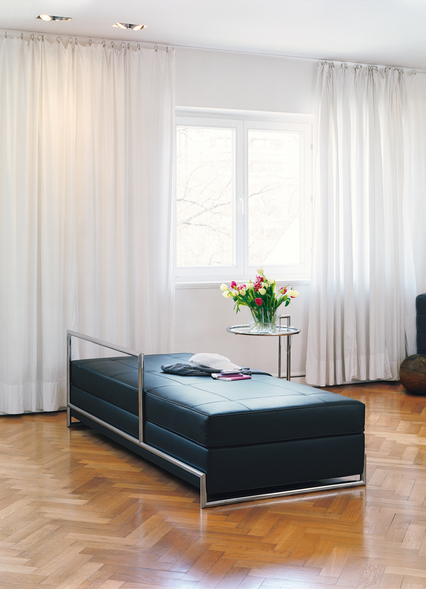 ClassiCon E1027 Adjustable Table Beistelltisch im Wohnzimmer mit schwarzer Liege und Tulpenstrauß.