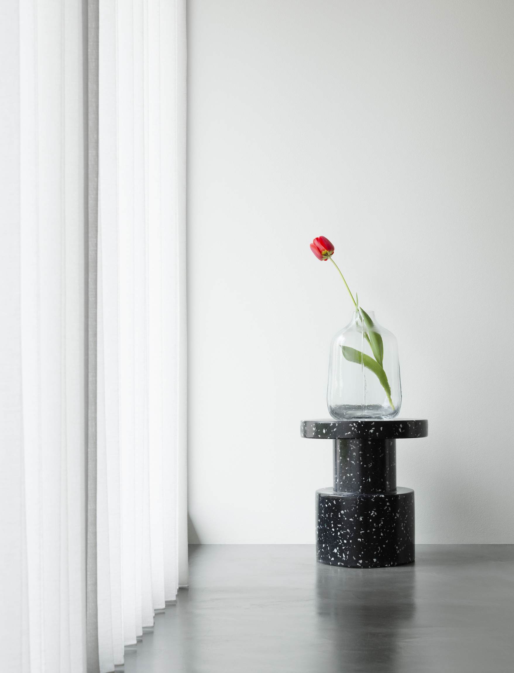 Normann Copenhagen Bit Stool Hocker in Schwarz-Weiß mit Vase und roter Tulpe.