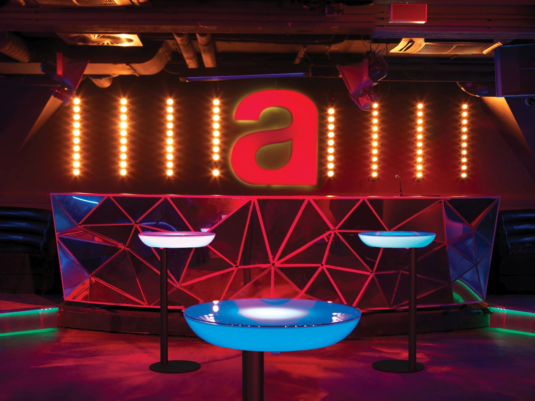 Moree Lounge M105 Leuchttisch/Stehtisch im Ambiente einer Bar mit farbiger Beleuchtung für den Außenbereich.