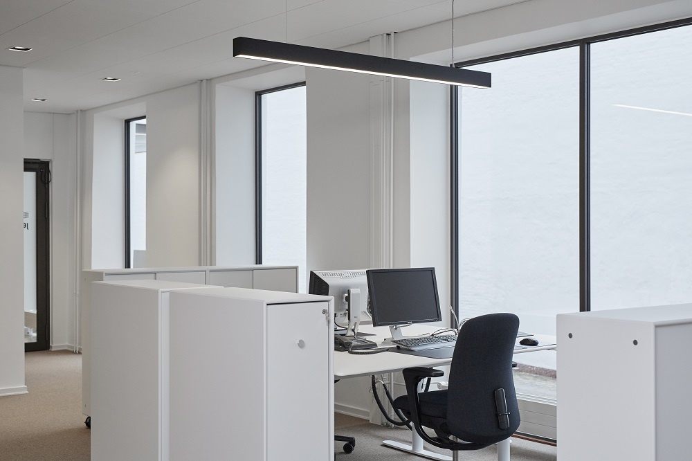 Büro mit weißem Montana Cargo Modul 80 Schrank-System, Schreibtisch, Bürostuhl und großen Fenstern.