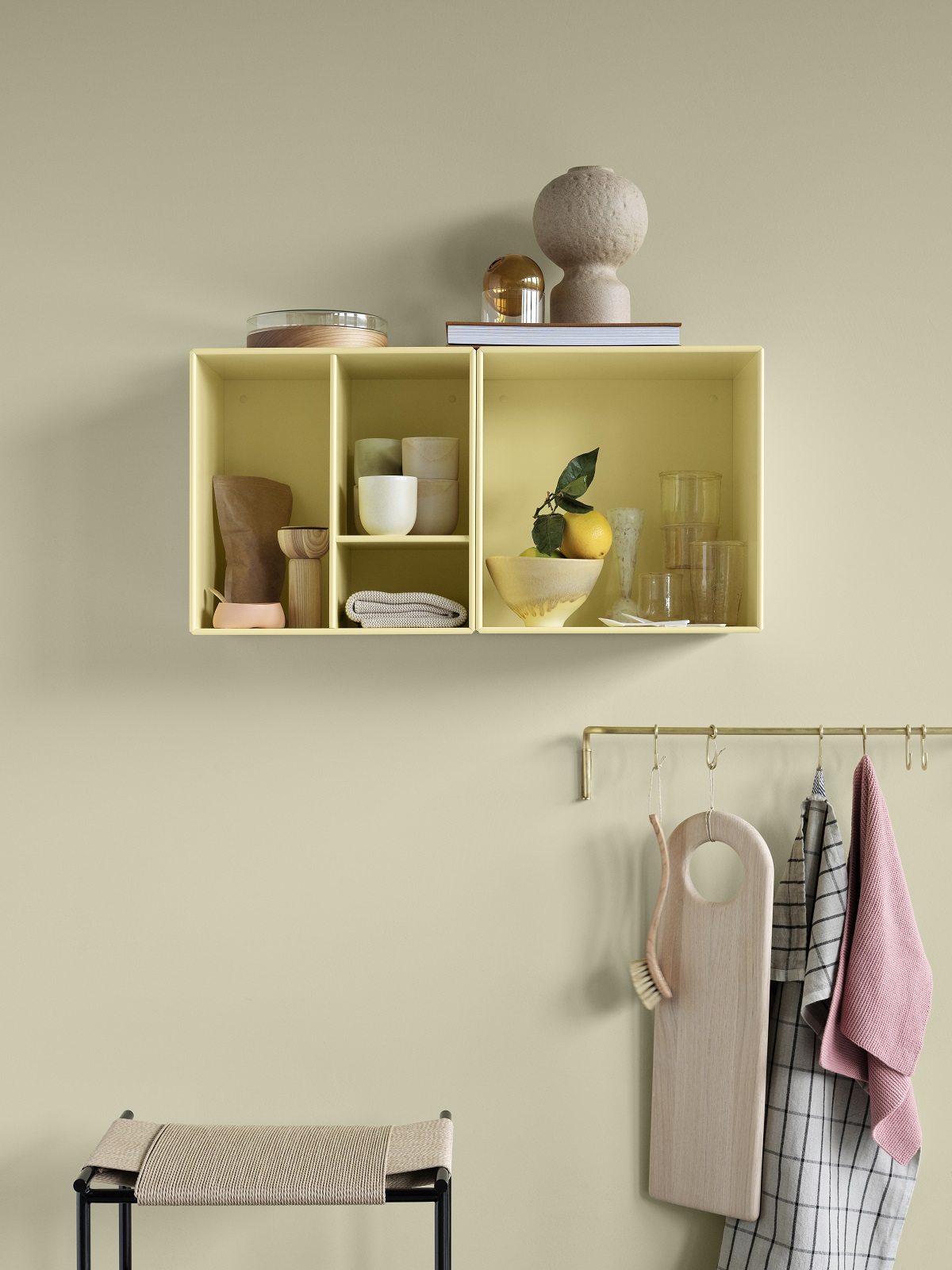 Gelbes Montana Mini Modul mit Fächern an der Wand, dekoriert mit Geschirr und Deko-Objekten.
