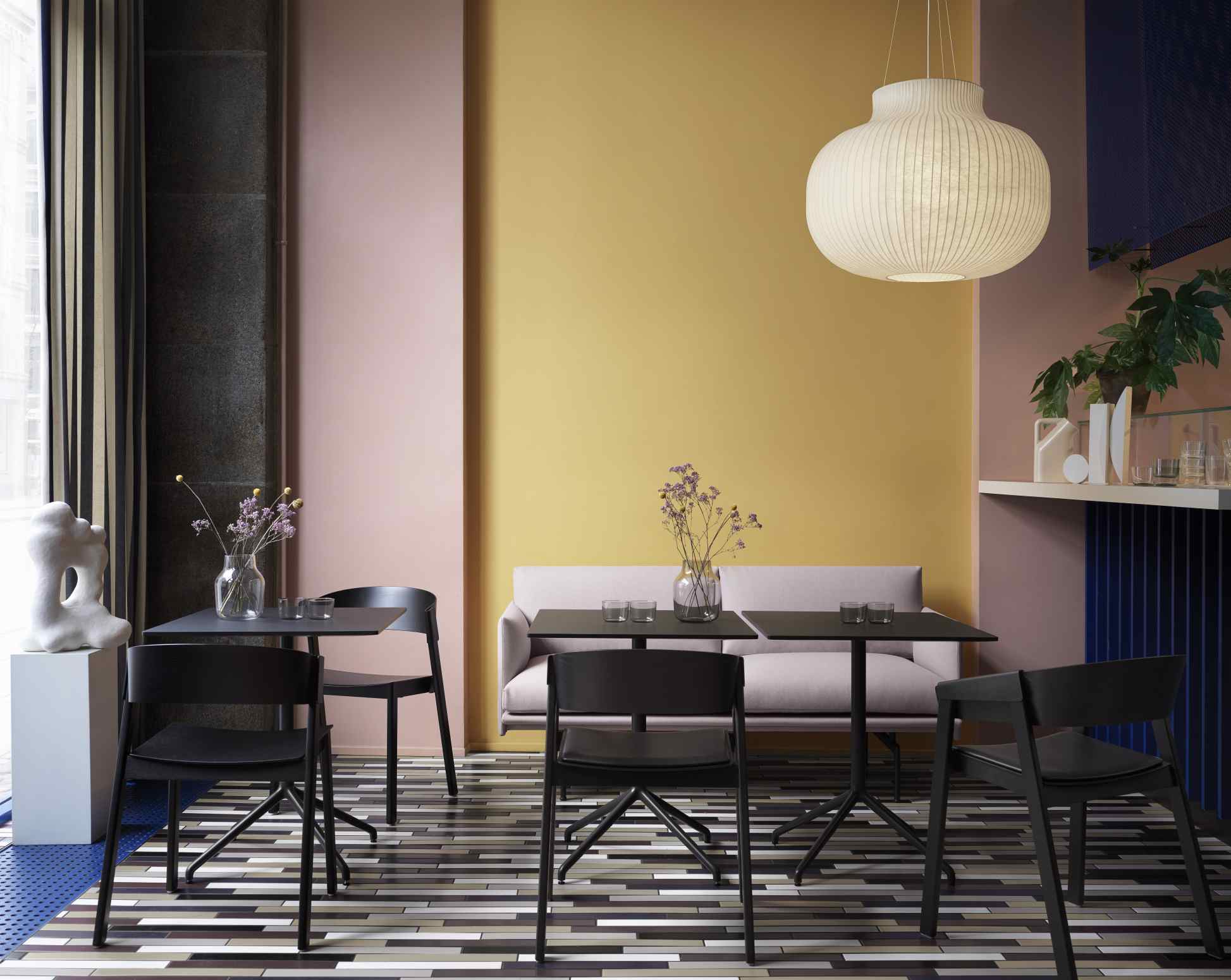 Helle Muuto Strand Pendelleuchte über Esstisch mit schwarzen Stühlen in modernem Interieur.