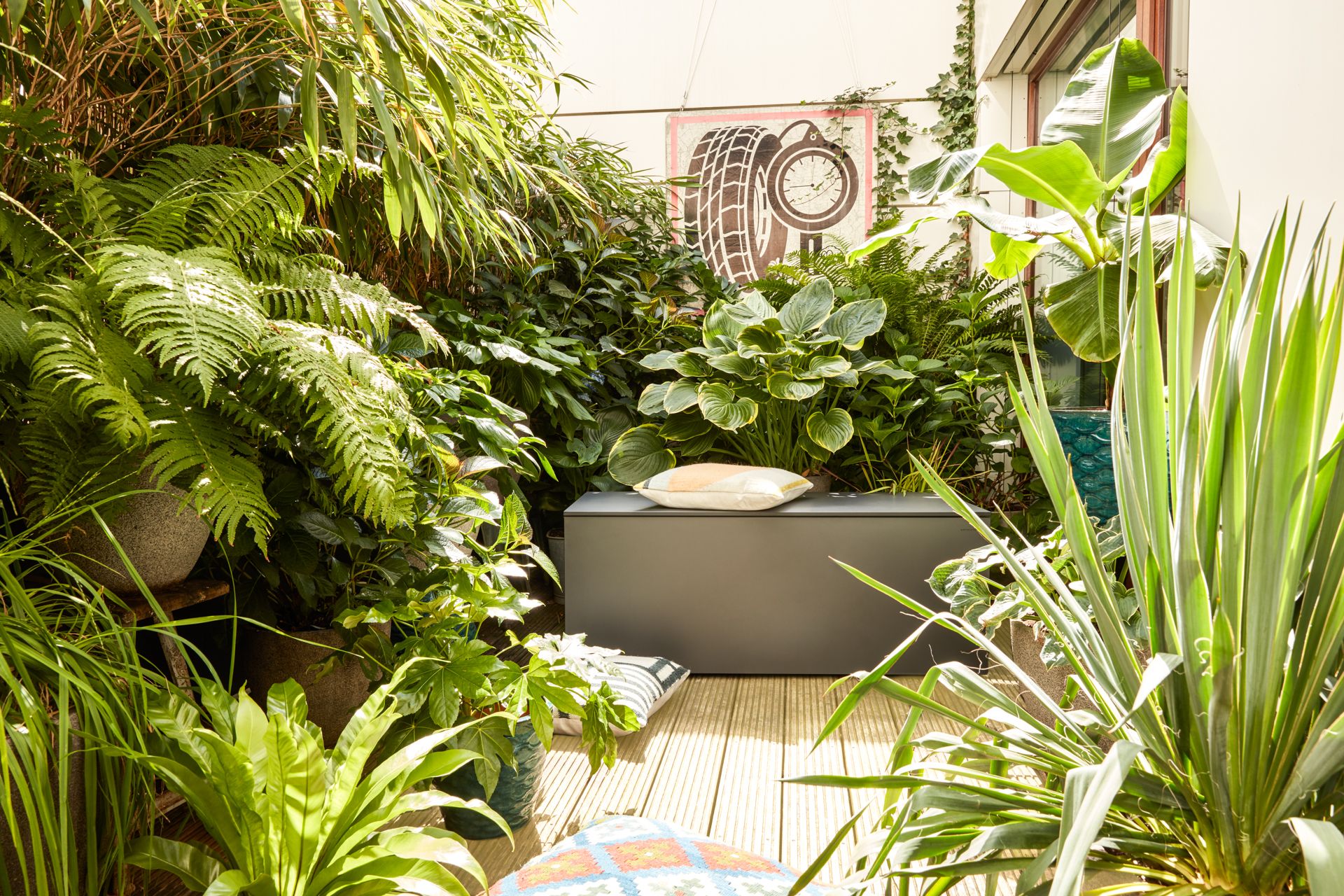 EL Pecho Kissentruhe von Conmoto auf einer begrünten Terrasse mit Kissen und Pflanzen.