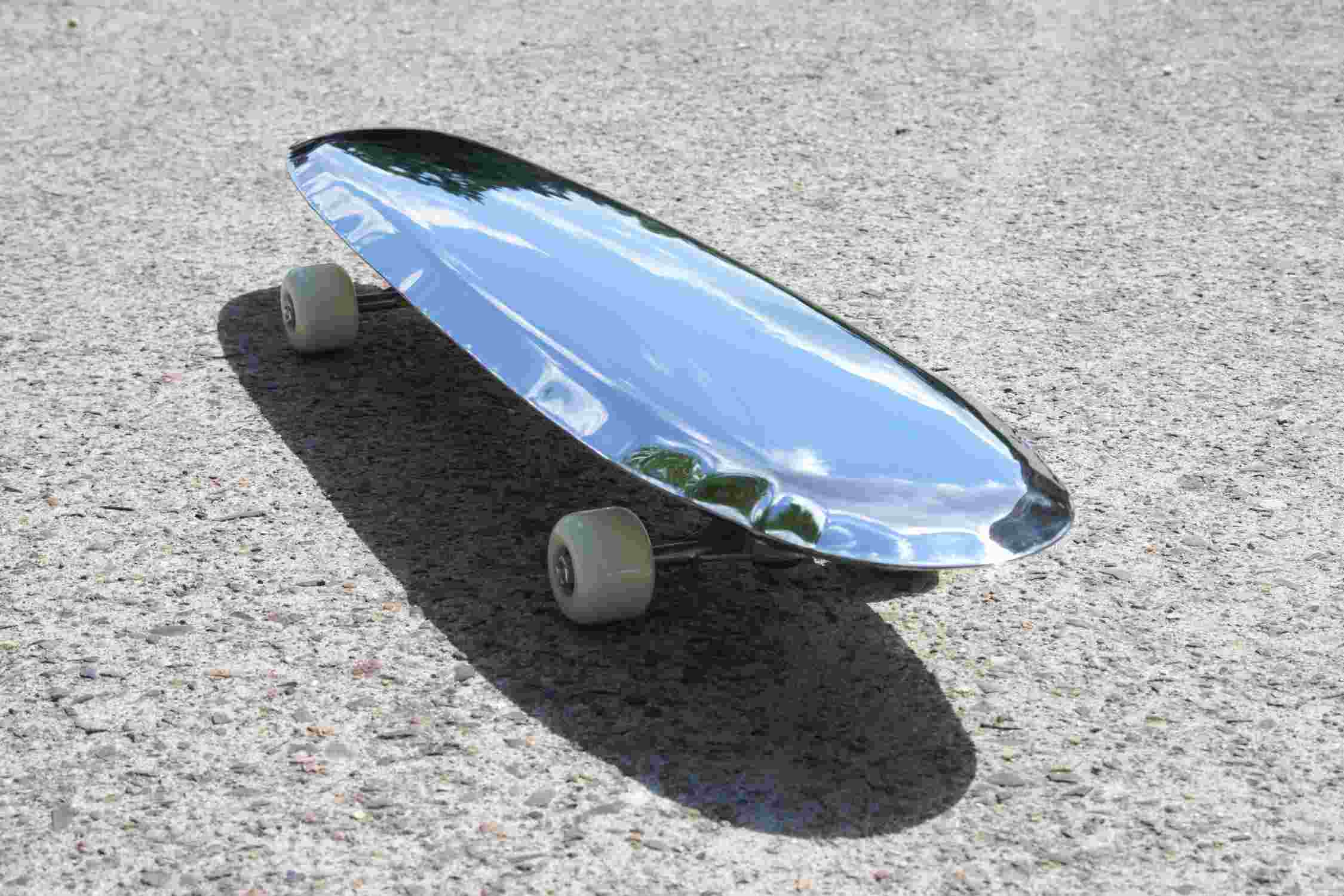 Bolid Spiegel von Zieta, ein glänzendes, reflektierendes Skateboard aus Metall auf Asphalt.