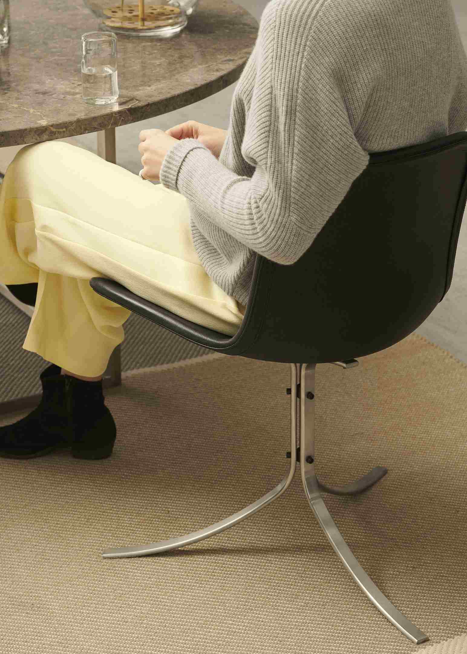 Person sitzt auf einem schwarzen PK9 Stuhl von Fritz Hansen am Esstisch.