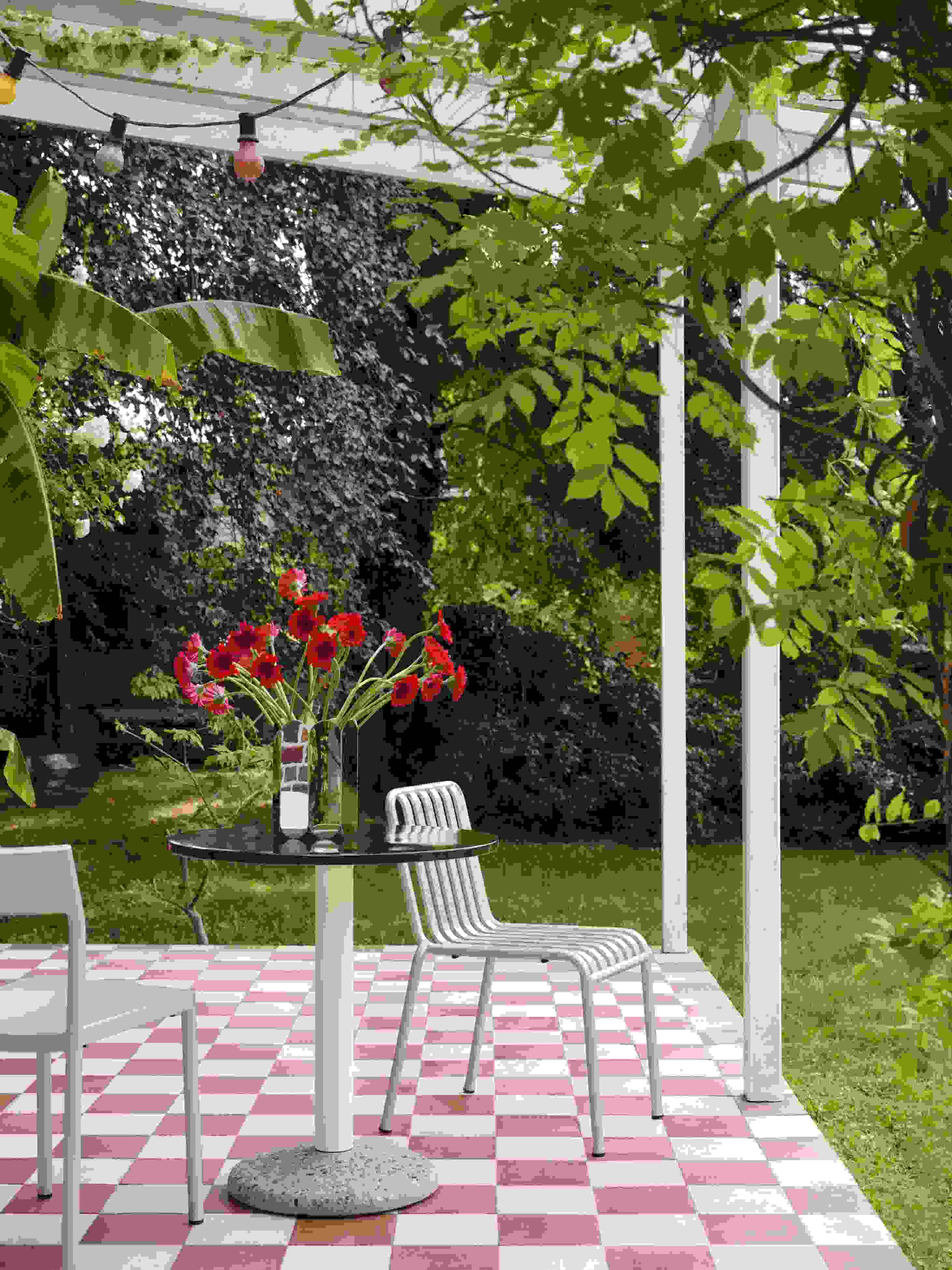 Helle Terrasse mit Hay Stühlen, rundem Tisch mit Blumen in der Arcs Vase L Mirror.