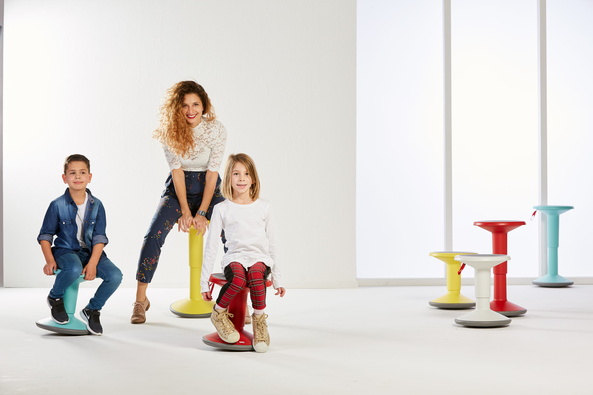 Kinder und Erwachsene sitzen auf bunten UP Junior Edition Kinderhockern von Interstuhl vor hellem Hintergrund.
