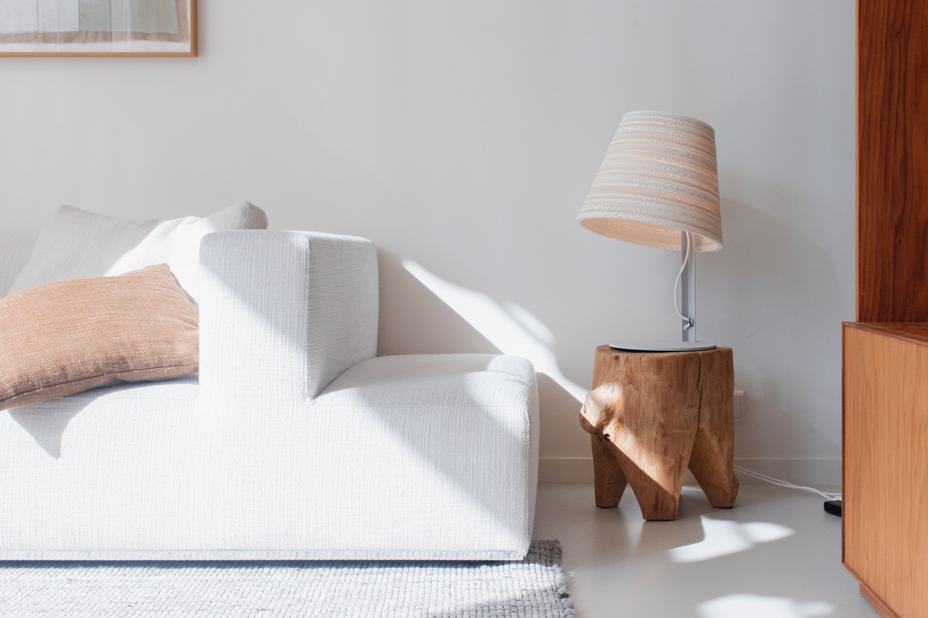 Tilt Tischlampe Scraplights von Graypants in Weiß auf einem Holzhocker neben einem weißen Sofa.