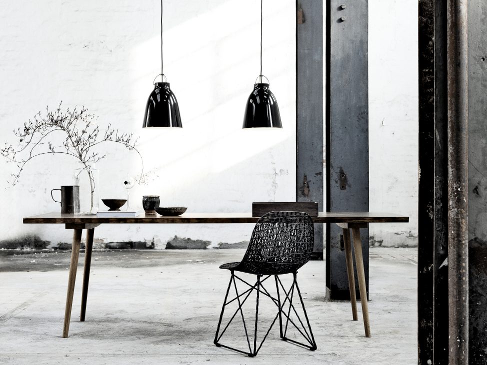 Zwei schwarze Caravaggio Pendelleuchten von Fritz Hansen über Esstisch mit Stuhl in Loft-Atmosphäre.