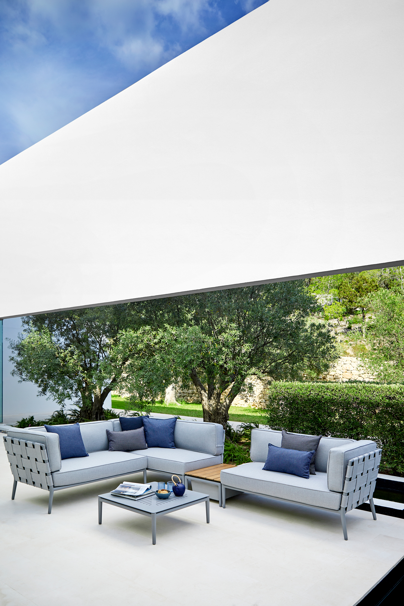 Conic AirTouch Modulsofa: Hellgraues 2-Sitzer Outdoor Sofa von Cane-Line mit blauen Kissen und Beistelltisch.