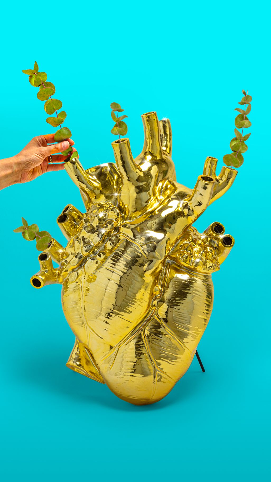 Goldene Love in Bloom Vase in Herzform mit Eukalyptus auf blauem Hintergrund. Dekorative Design-Vase.