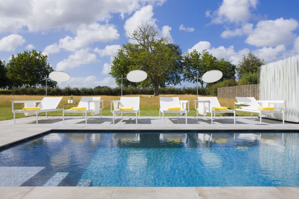 Weiße Sol + Luna Sonnenliegen von Extremis am Pool mit Sonnenschirmen und gelben Handtüchern.
