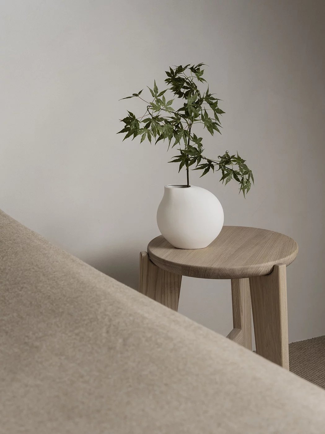 Eli Hocker von Blomus: Runder Sitzhocker aus hellem Holz mit Pflanze in Vase.