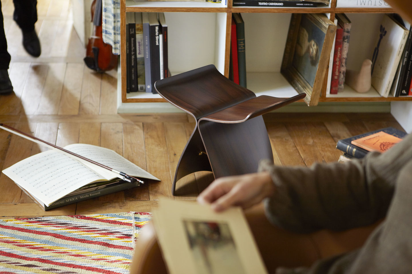 Vitra Butterfly Stool Hocker aus dunklem Holz im Wohnzimmer mit Bücherregal.