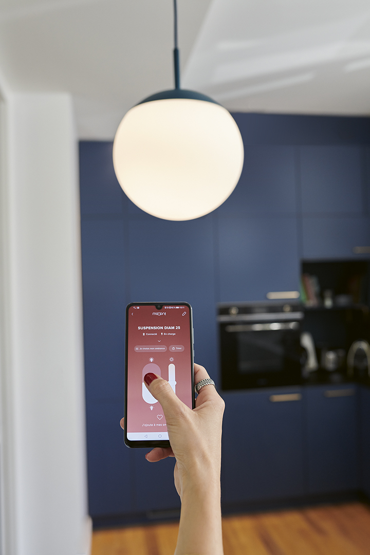 Mooon Suspension Pendelleuchte: Frau steuert die Helligkeit der runden, weißen Hängelampe per Smartphone-App in der Küche.