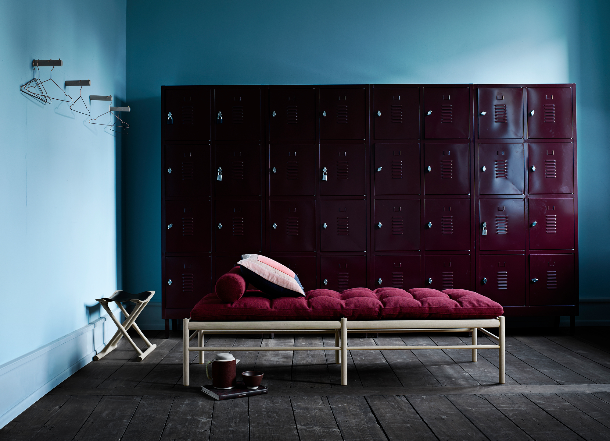 OW150 Daybed von Carl Hansen: Liege mit roter Polsterung, Kissen und hellem Holzgestell vor Spinden.
