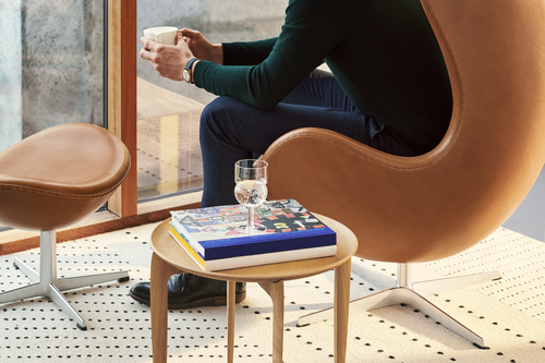 Mann sitzt in braunem Ledersessel mit Beistelltisch, Buch und Glas. Designermöbel für Wohnzimmer.