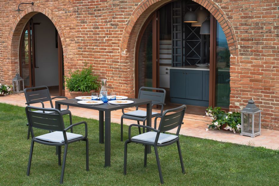 Nova Tisch von Emu, ein quadratischer Gartentisch mit vier Stühlen auf einer grünen Rasenfläche.