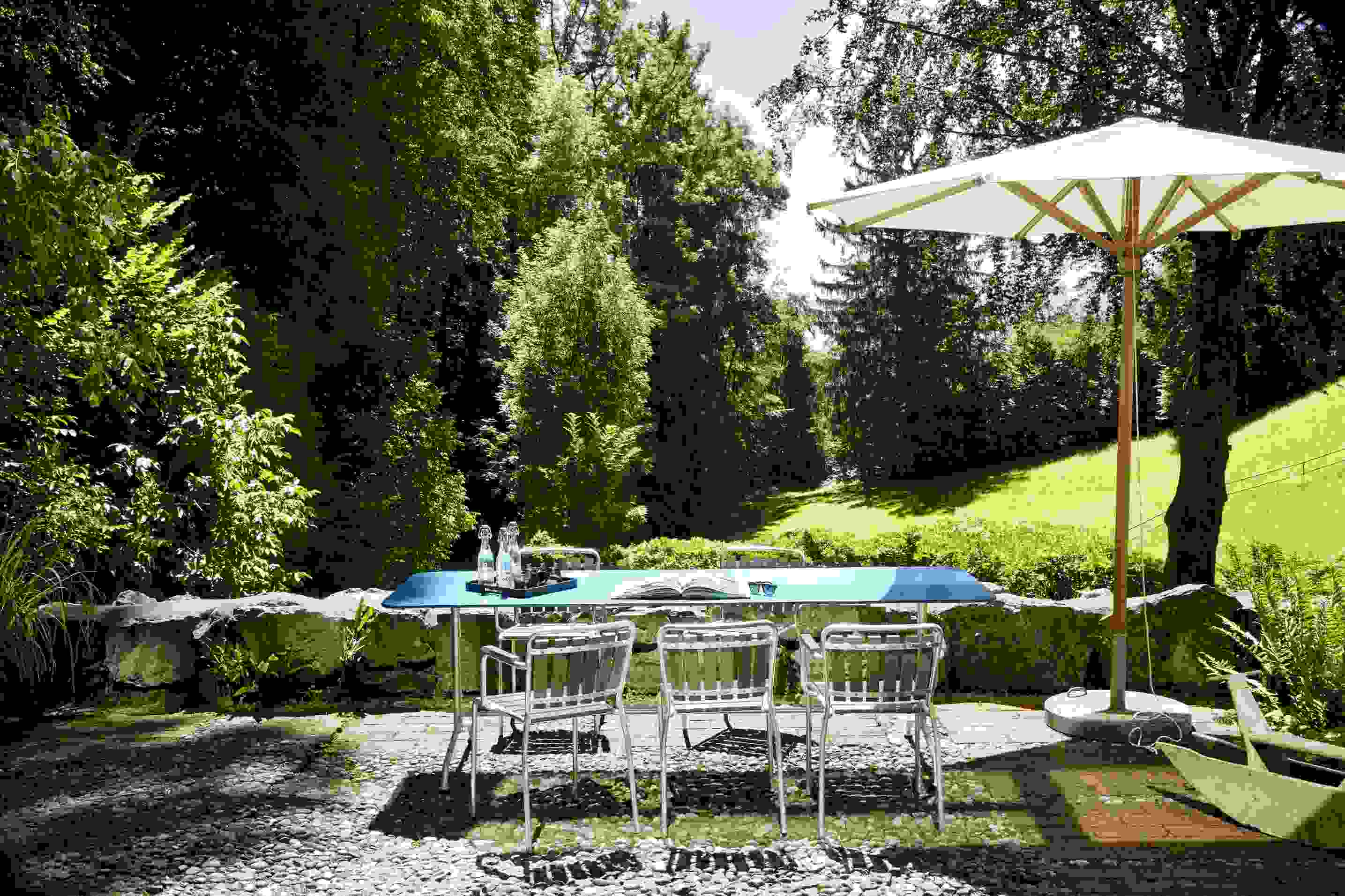 Gelber Haefeli Esstisch Outdoor mit Stühlen und Sonnenschirm im Garten. Hochwertiger Gartentisch für stilvolle Outdoor-Momente.