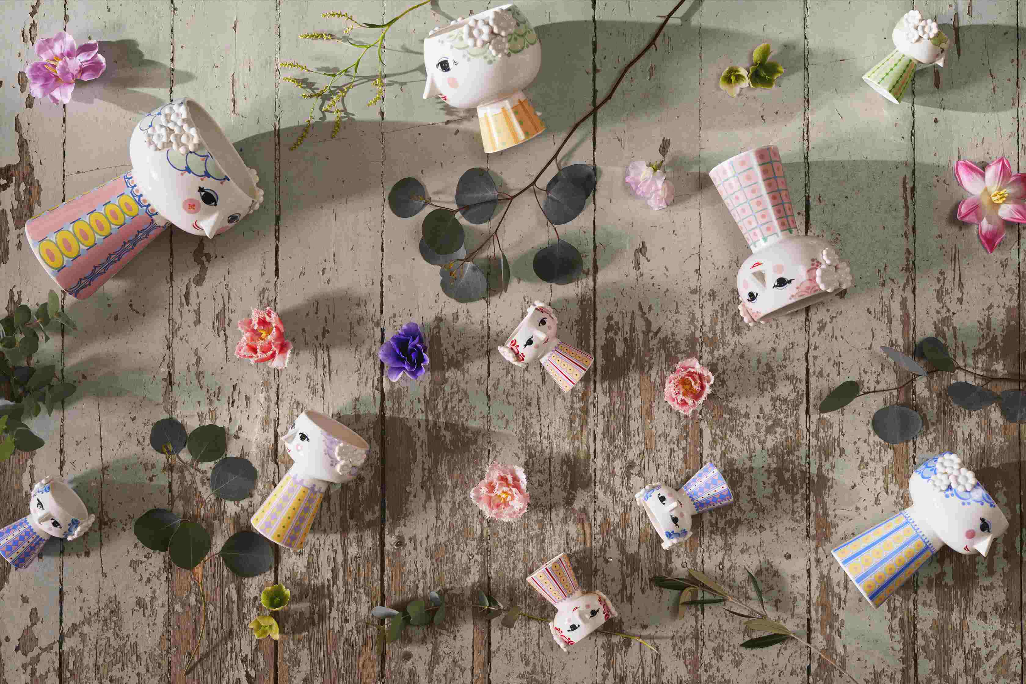 Verschiedene Keramik-Blumentöpfe im Gesicht-Design mit Blumen auf einem rustikalen Holztisch, dekorative Pflanzgefäße für Zimmerpflanzen.