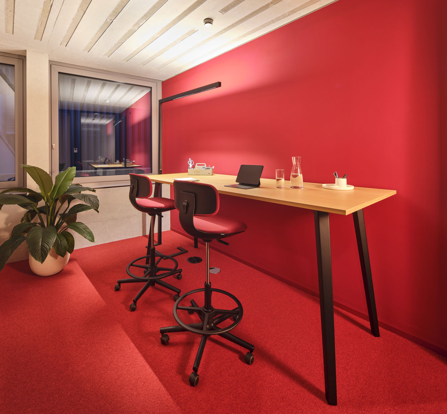 Zwei rote Vitra Rookie High Bürostühle an einem hohen Schreibtisch in einem modernen Büro.