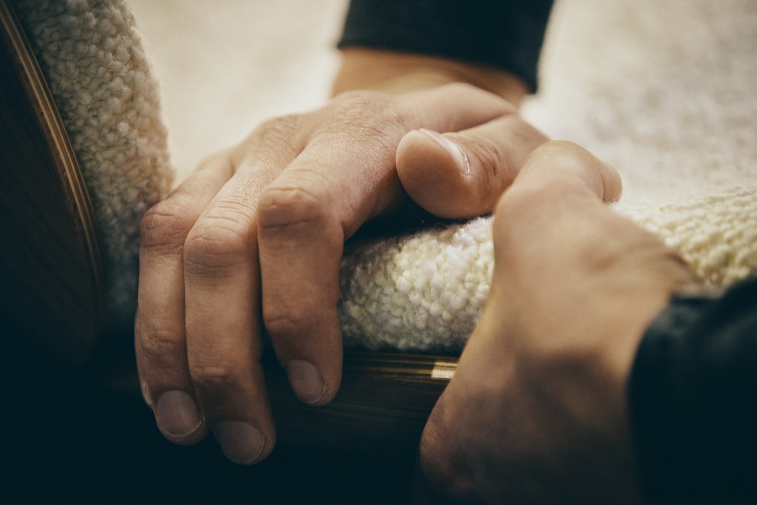 Nahaufnahme einer Hand, die einen Stuhl mit weichem, weißem Lammfellbezug berührt. Komfort und Qualität.