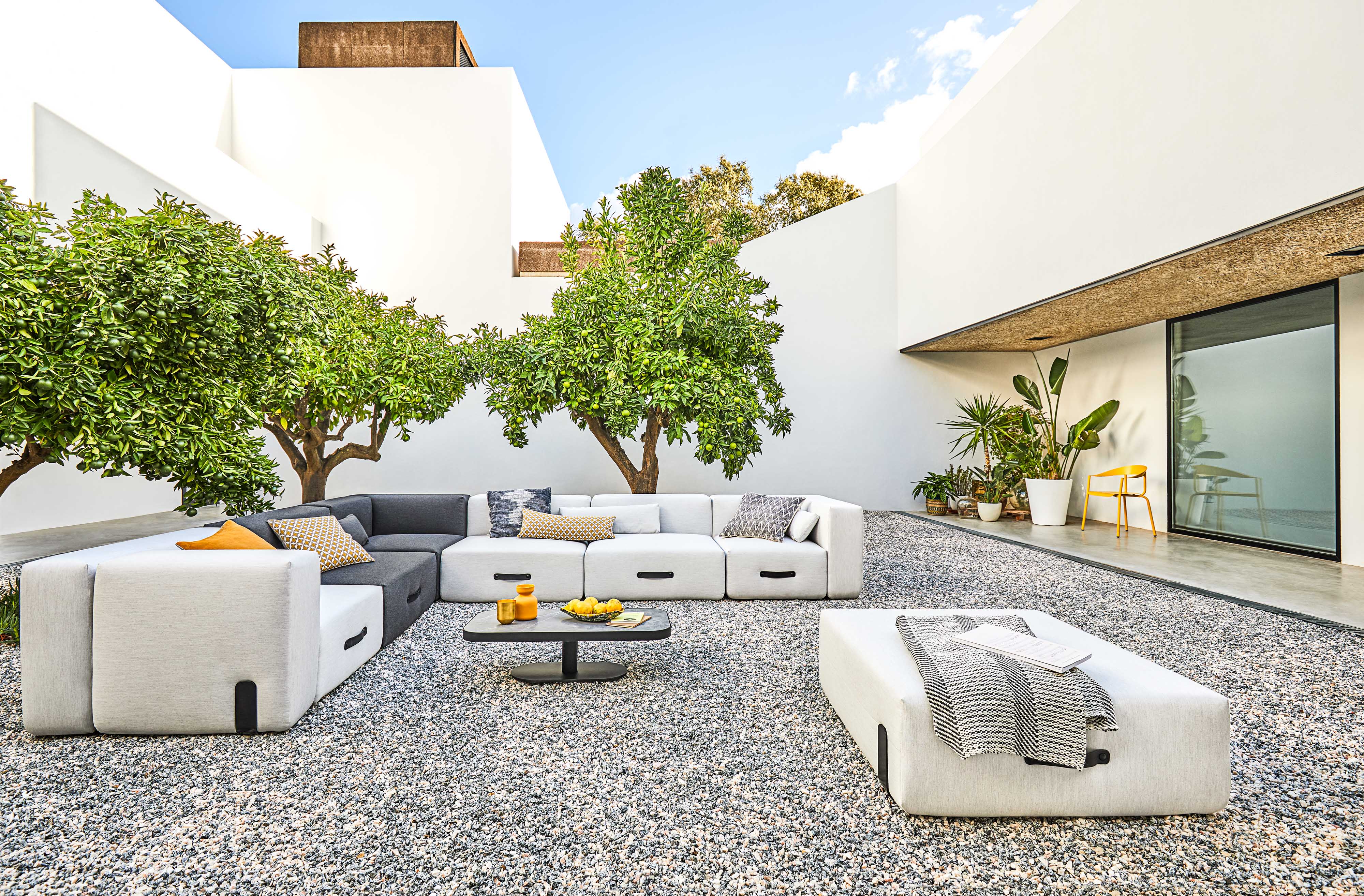 Miami Outdoor Sofa Lounger Conmoto auf Kiesterrasse mit Beistelltisch, Obstschale und mediterranen Pflanzen.