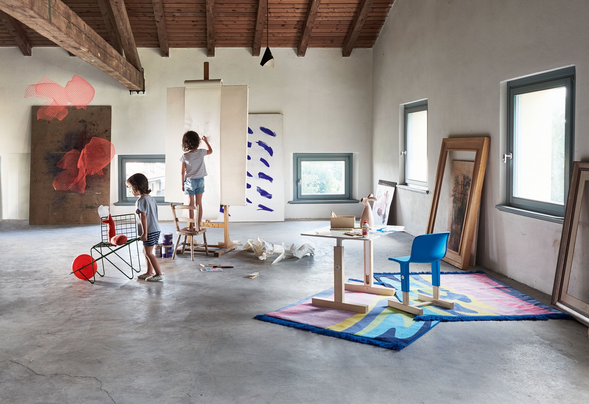 Heller Raum mit Kindern beim Malen, im Vordergrund blauer Little Big Chair Kinderstuhl von Magis.