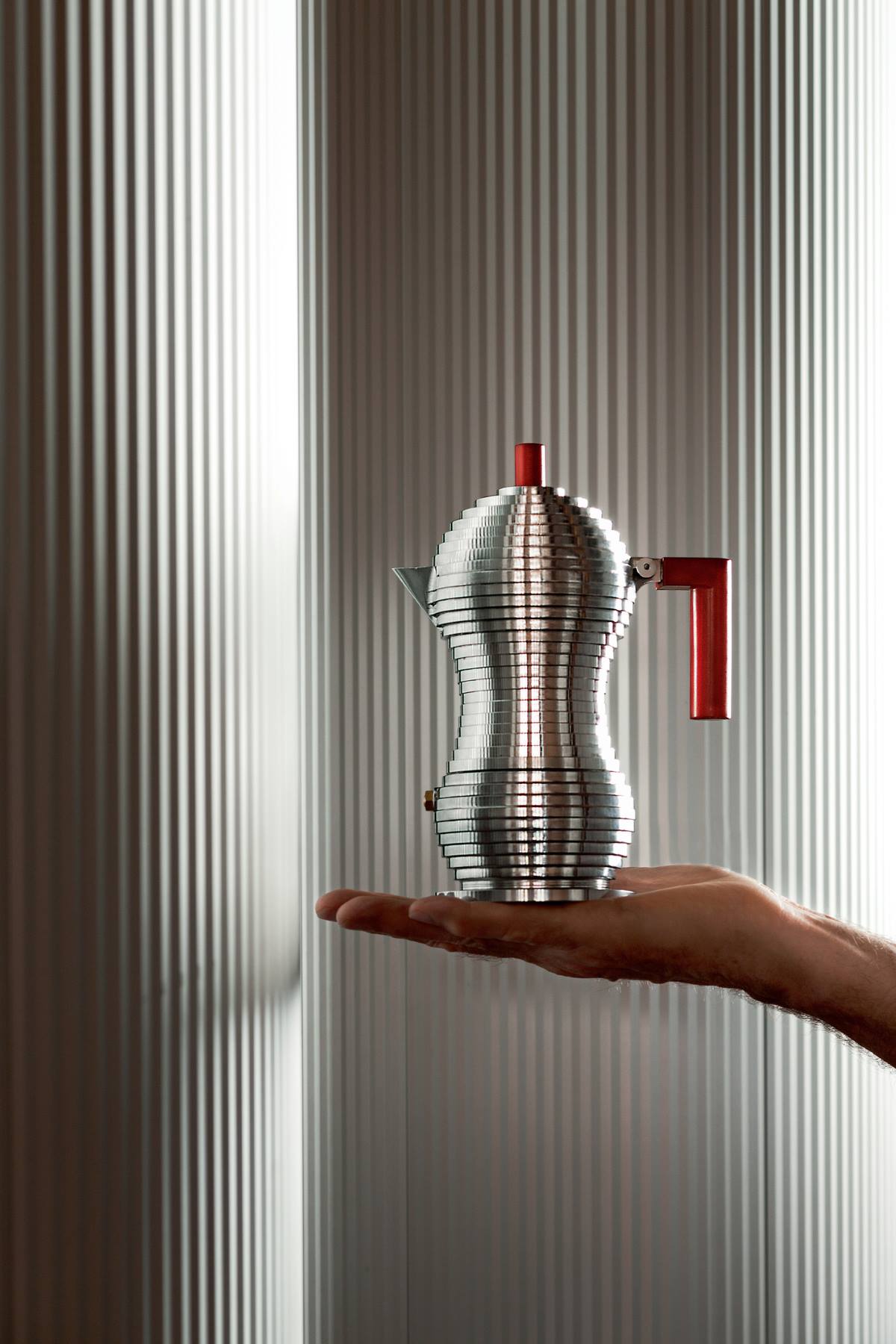 Alessi Pulcina Espressokocher MDL02 auf einer Handfläche, modernes Design, silberfarben mit rotem Griff.