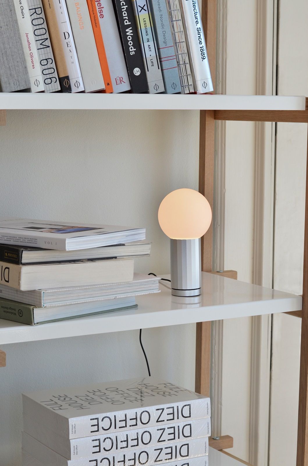 Detailaufnahme des Hay Woody Shelving Column Regals mit Büchern und einer modernen Lampe.