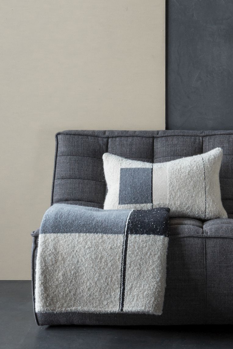 Urban Überwurf von Ethnicraft: Grauer Wollüberwurf und passendes Kissen mit geometrischem Muster auf Sofa.