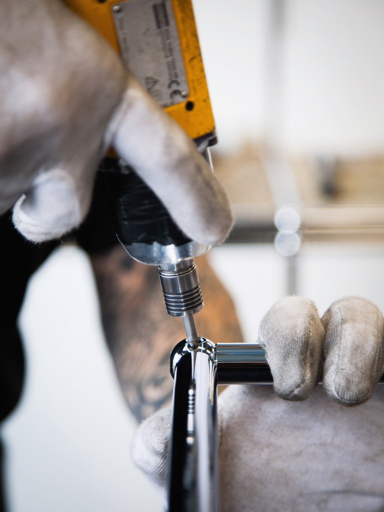 Montage eines verchromten Möbelstücks mit Akkuschrauber und Handschuhen. Möbelbau, Handwerker, Chrom.